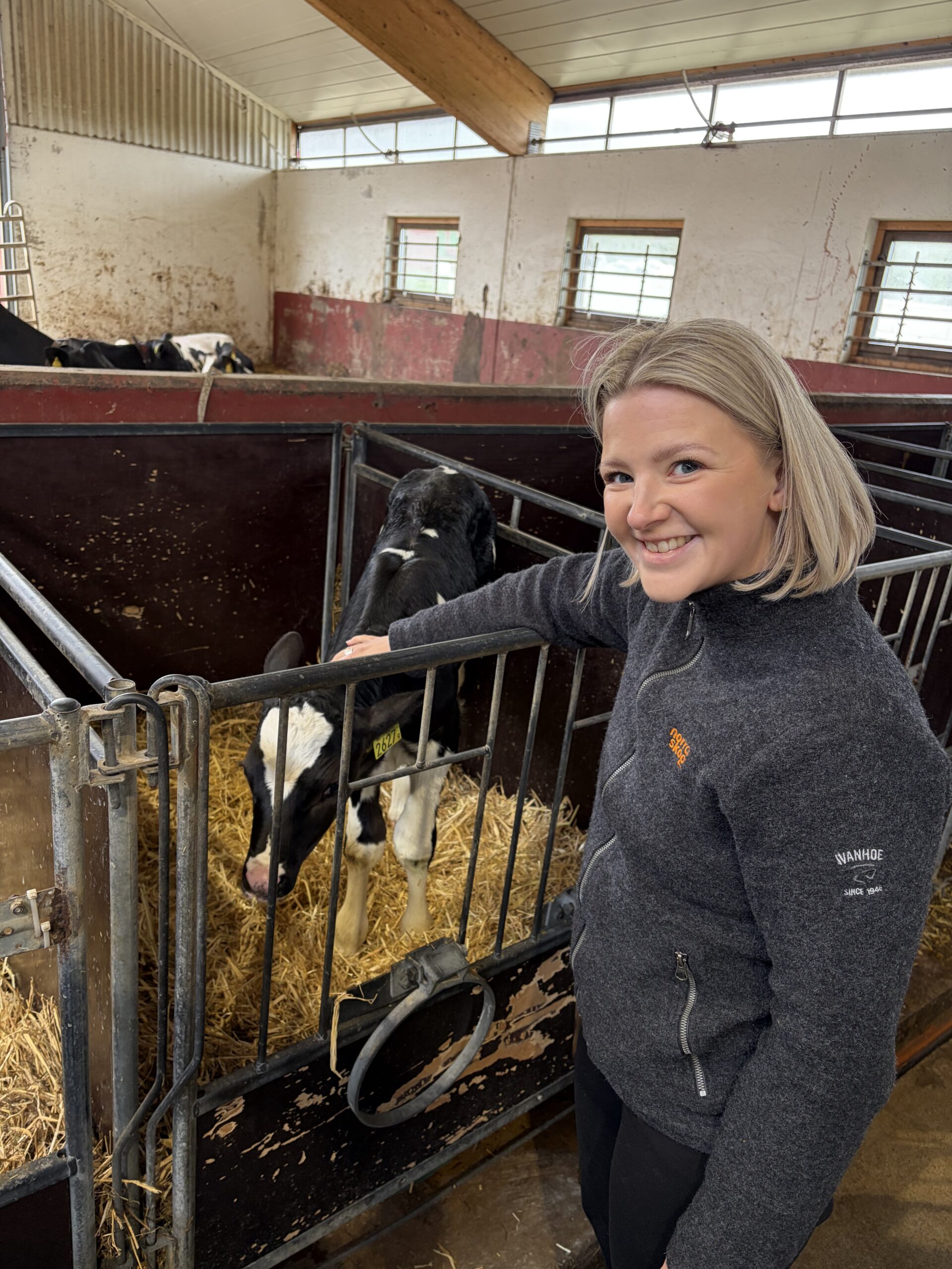 Julia klappar en kalv på ett lantbruk i Flarken. Hon ler.